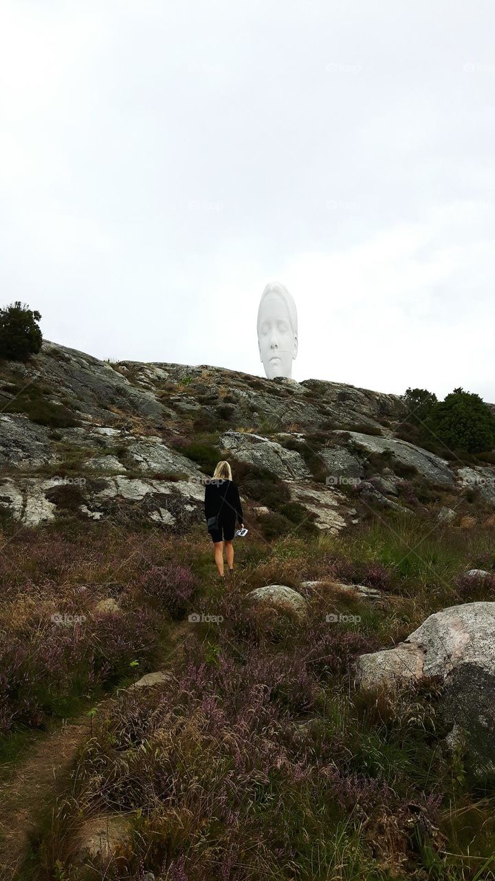 Woman walking up a hill towards a white sculpture head