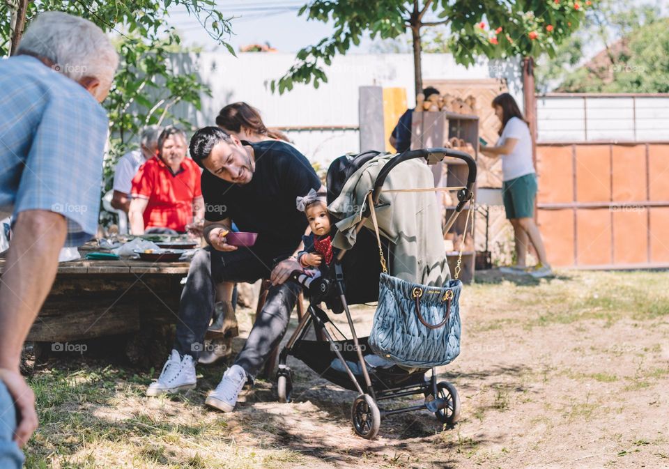 Father and daughter. Young baby girl, in a stroller, being fed by her father while being outside at an event.