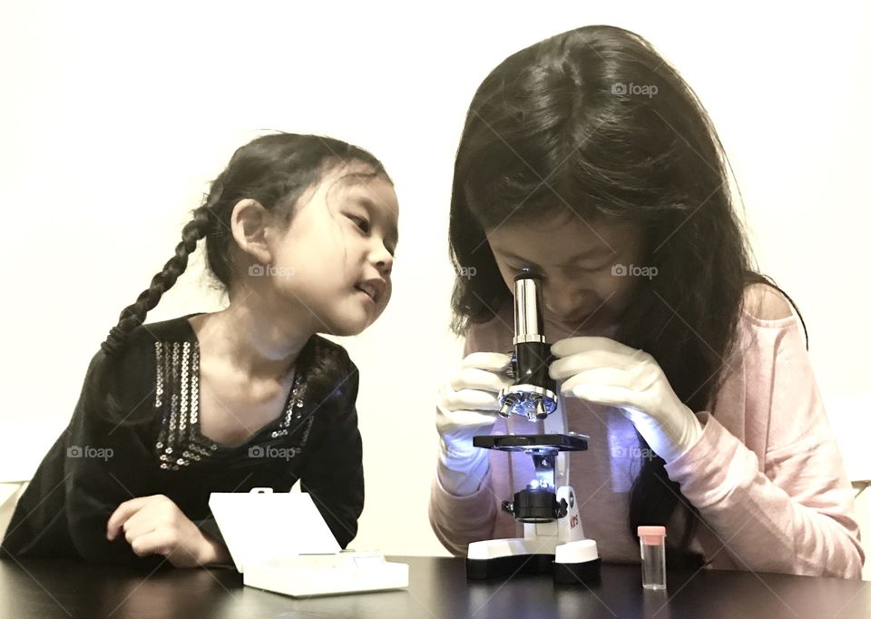 Two schoolgirls with microscope on desk