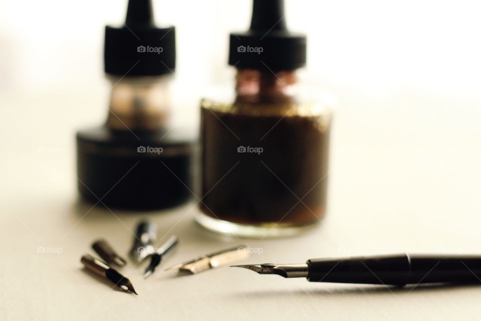 Arts & Crafts Supply - blurred view of a black and sepia ink bottles with various-sized metal nibs, nib in holder on parchment paper