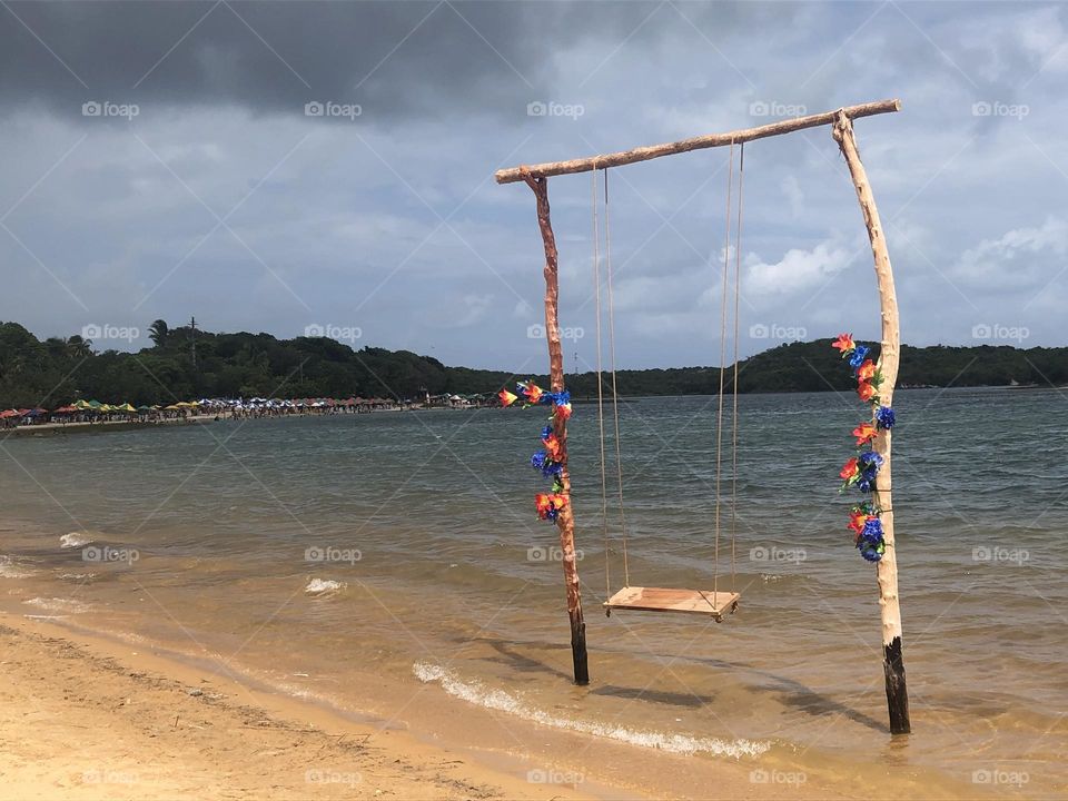 Swing at the sea water decorated with flowers on the beach 