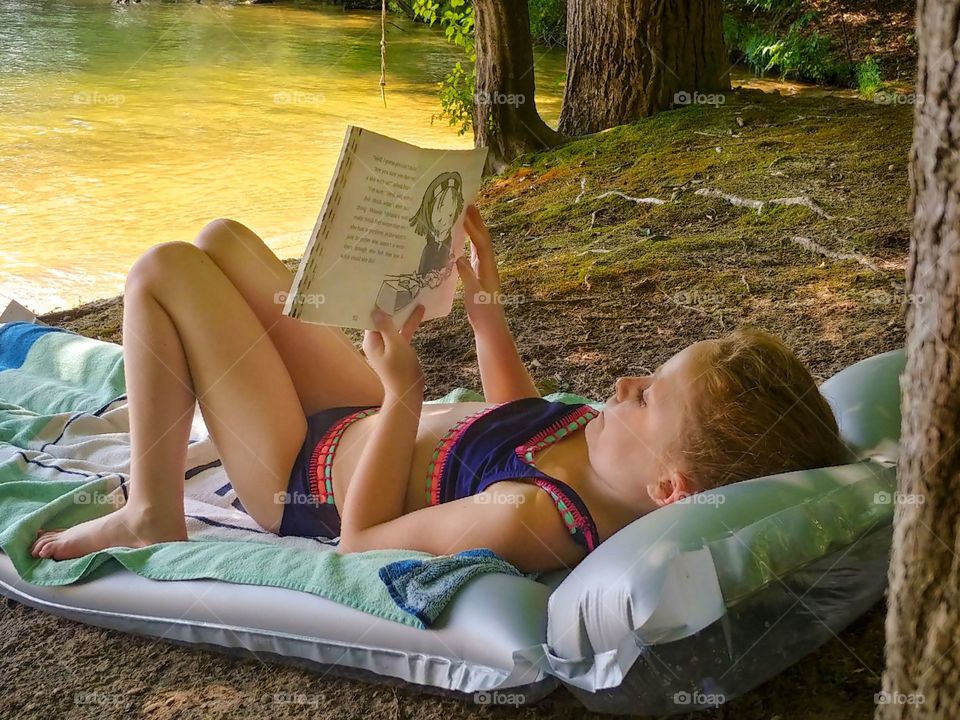 A child lays in the woods and reads a book.