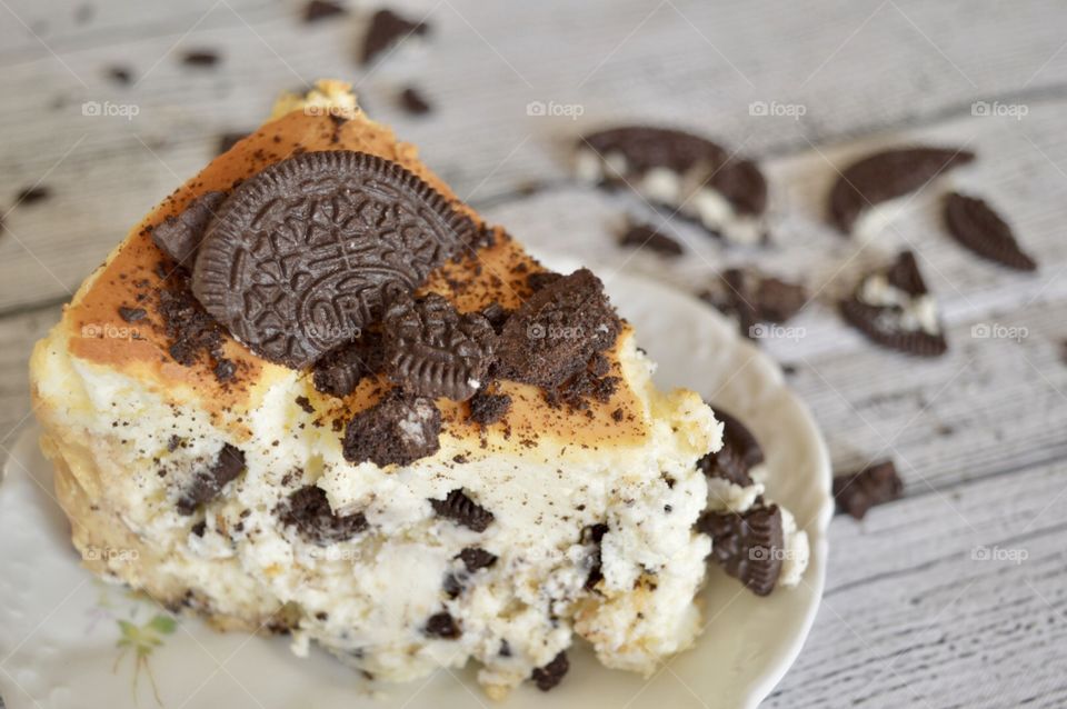 Oreo cookie cheesecake on a white plate with a white rustic background and cookie crumbles in the background