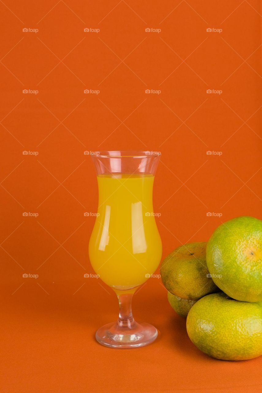 Oranges and glass with natural juice on orange color background