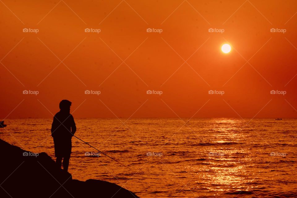 A man fishing in the ocean during an early morning sun rise 