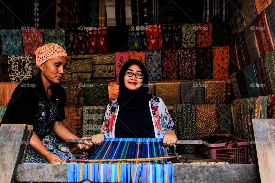 Portrait of a young woman sitting learning to weave cloth with traditional tools at a traditional cloth craft workshop in Sade village, with a happy expression, Lombok, Indonesia.