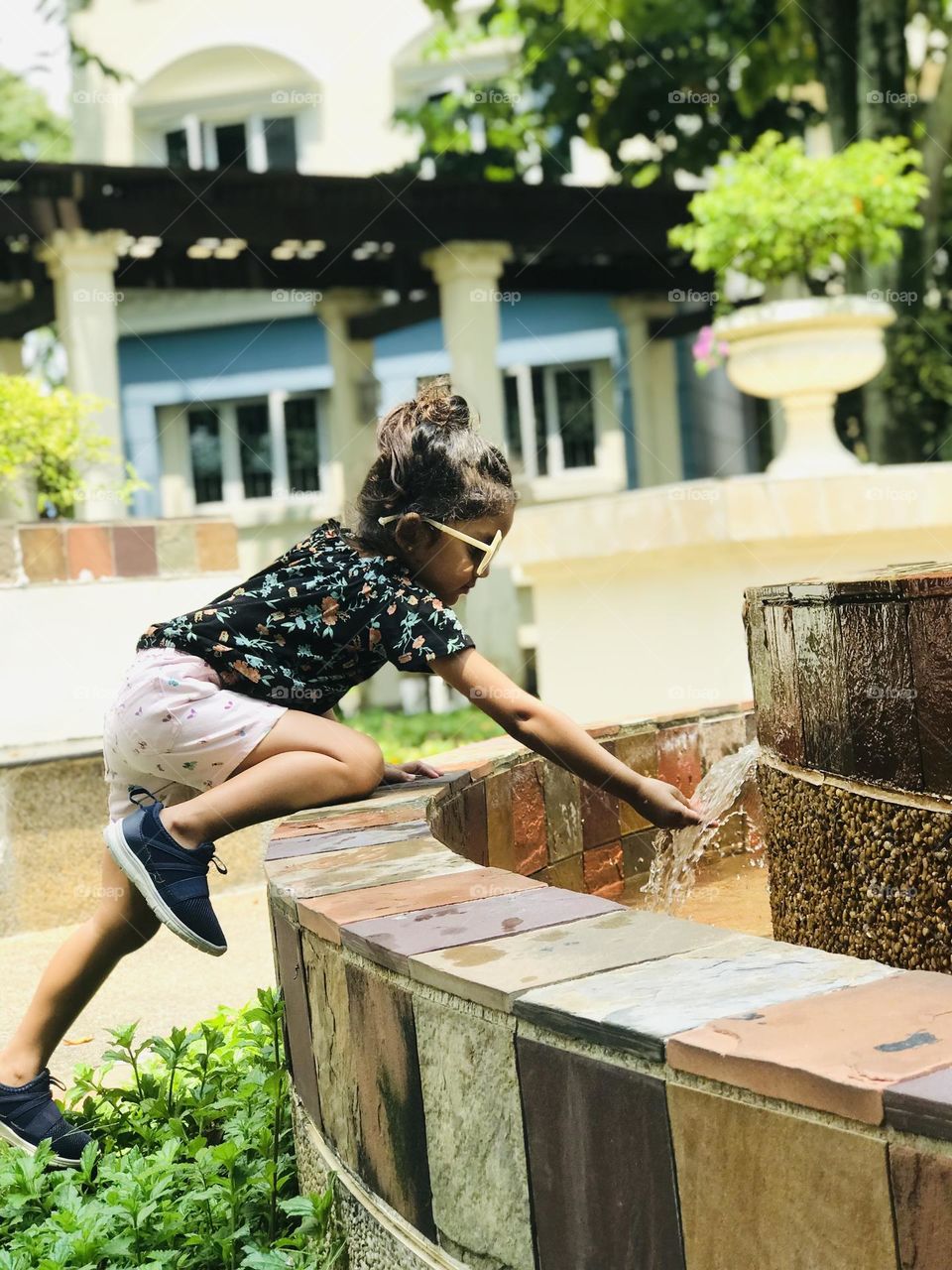 A pretty girl playing at water fountain in a summer outfits.