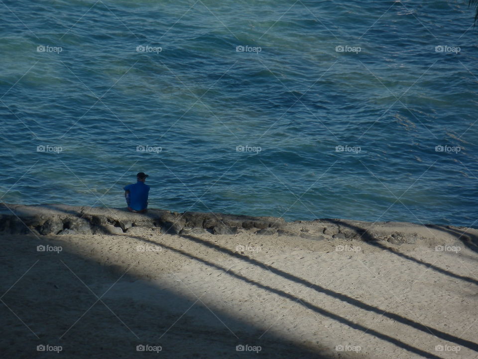 Peaceful moment man sitting in the shadows by the ocean in Hawaii, shadows of palm trees in the sun 