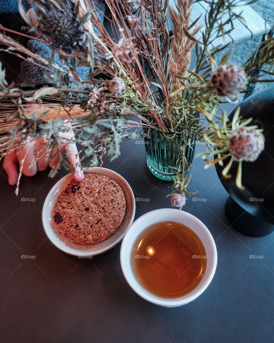 Cute and tender dry flowers in a little glass vase near the tea and cookies somewhere in a cozy cafe