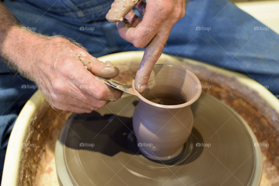 A craftsman making a clay pot on a pottery wheel. 
