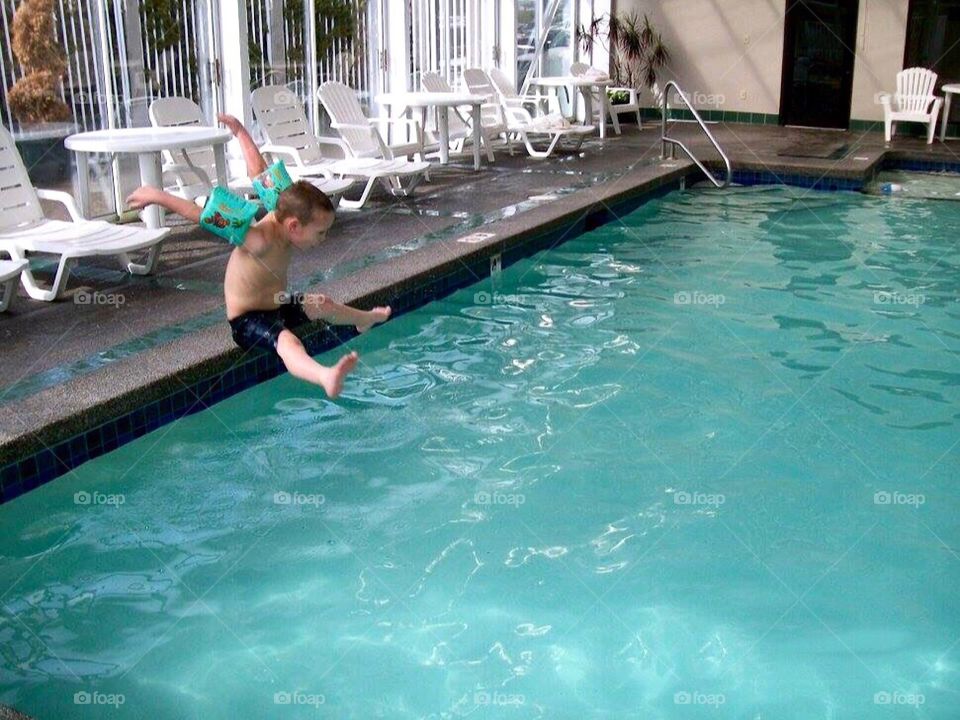 Young boy jumping into an indoor hotel pool while on vacation