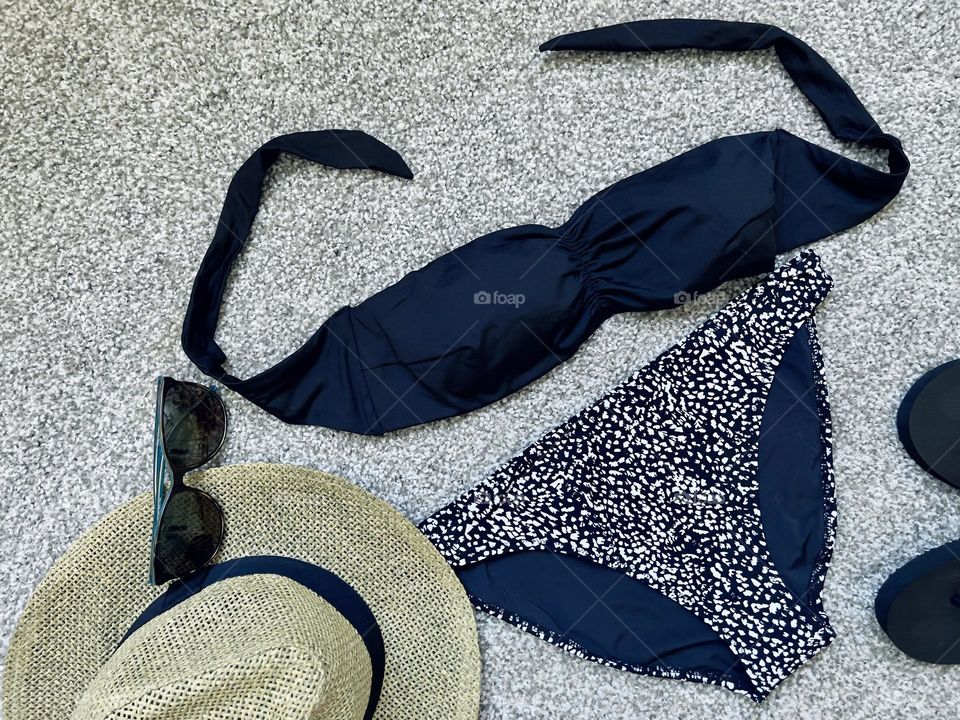 Black and white bikini next to straw hat, top view 