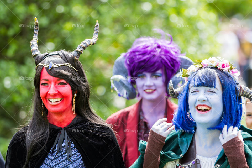 A group of cosplayers dressed as Critters with colourful face paints laughing together at a comic con event