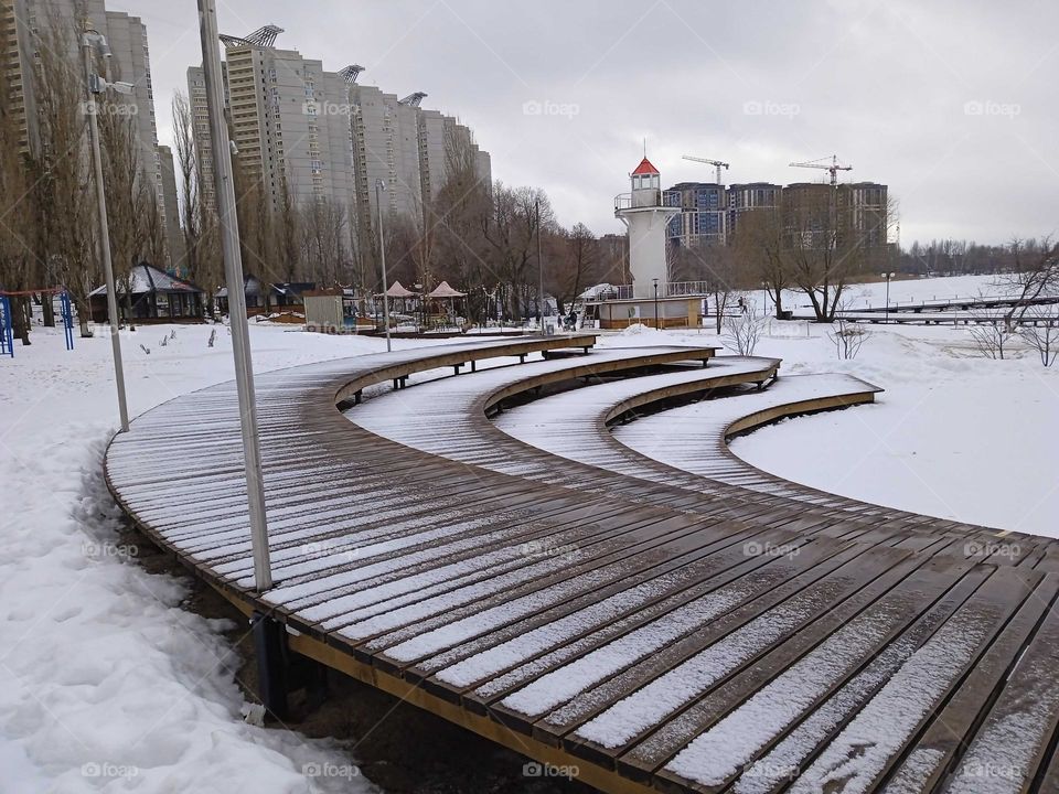 February, gloomy day, walking park near the river, seats covered with snow