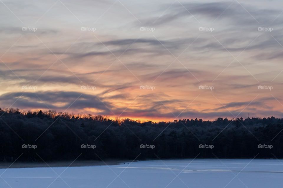 Beautiful sunset by frozen lake in winter, clouds looking like dark waves in the sky 