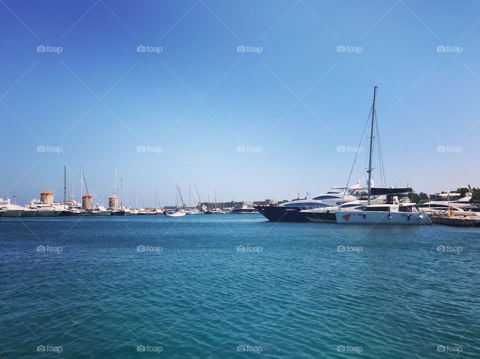 On the flat blue water of the harbor, a lot of yachts moored , in the clear blue sky without a cloud , a perfect blue background to make things stand out