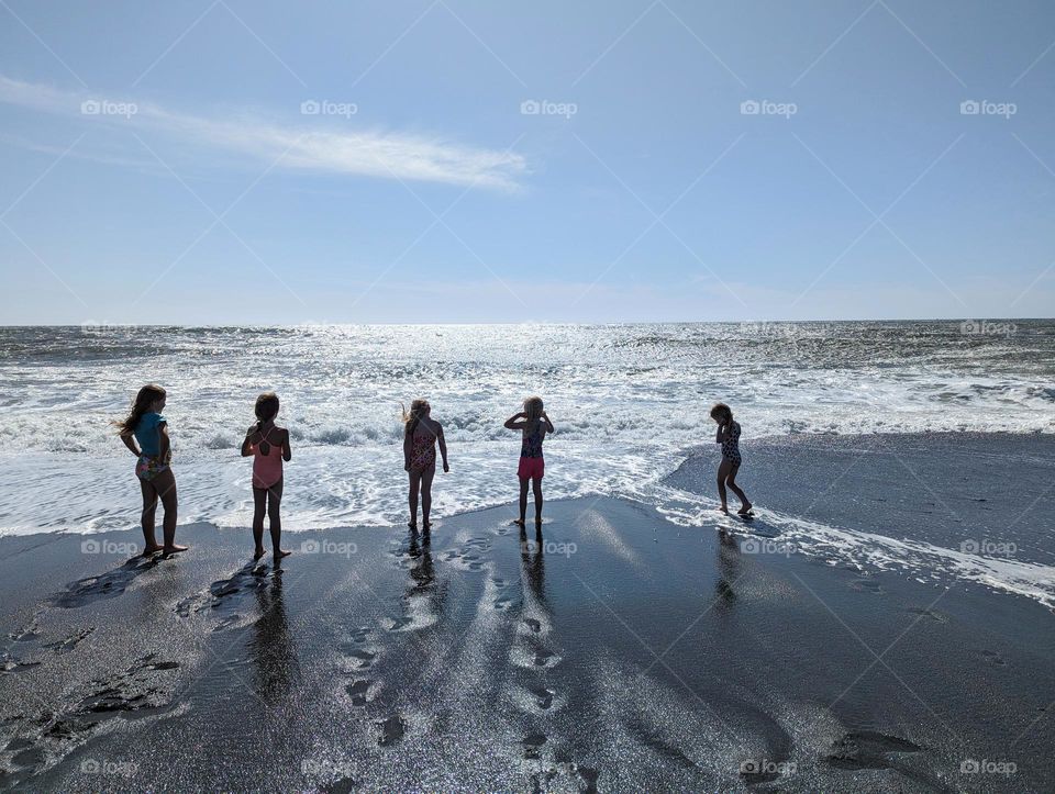 five kids silhouetted on the sandy ocean beach on a sunny day and beautiful shoreline with blue skies