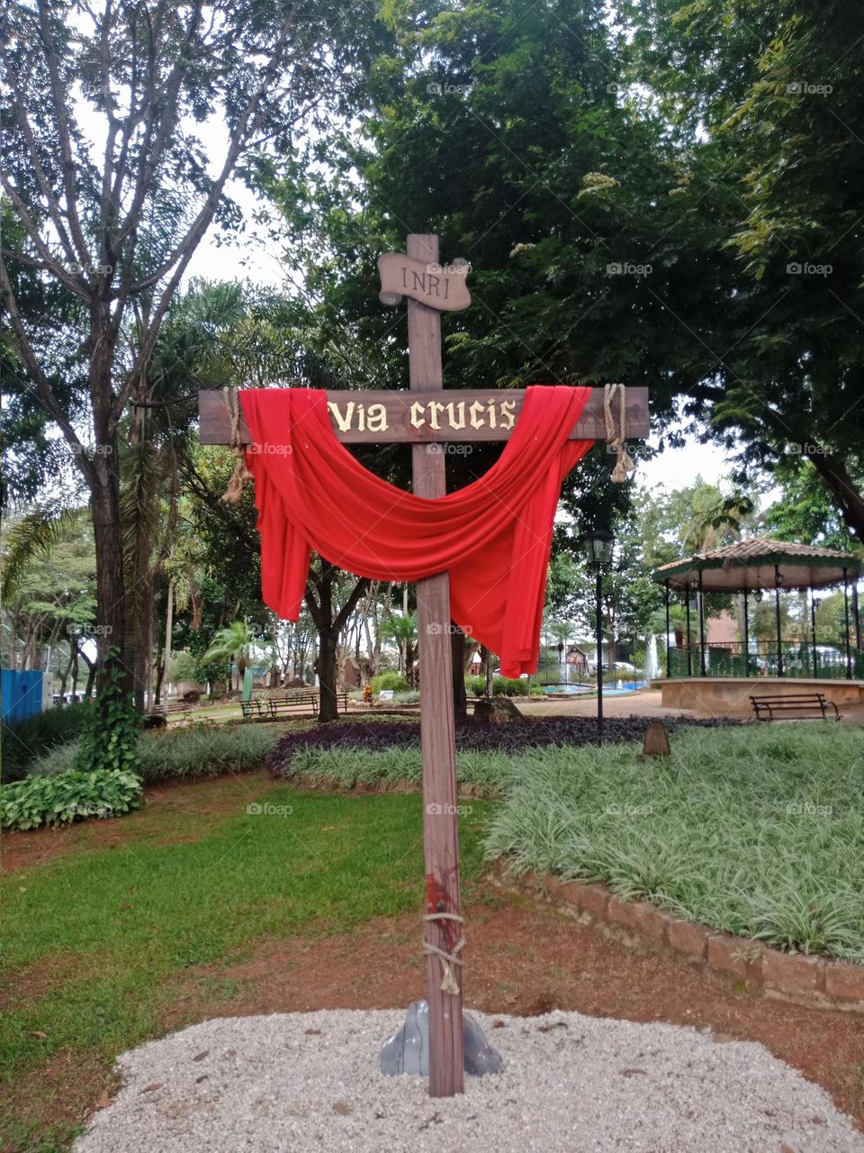 An empty cross in a garden, with a red cloth representing Jesus blood. Trees and plants.