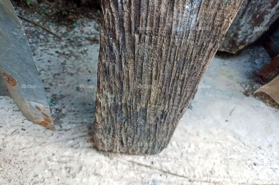 Close-up view of a piece of wood standing upright near a rusty metal object. The wood looks old and has discolored, perhaps due to weather or age