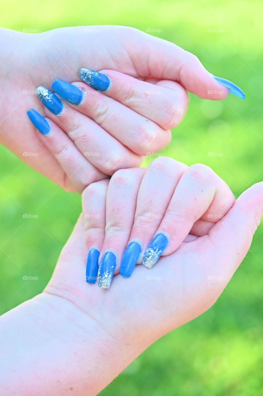 The blue fancy nails for the summer with a green blurry background 