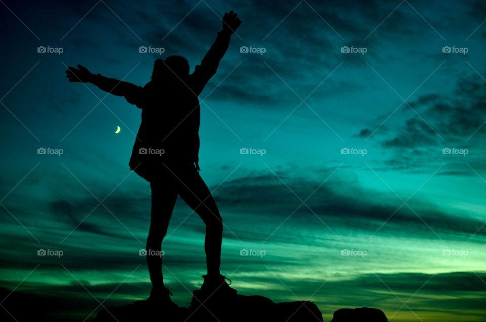 Woman standing on rock with arms raised at night