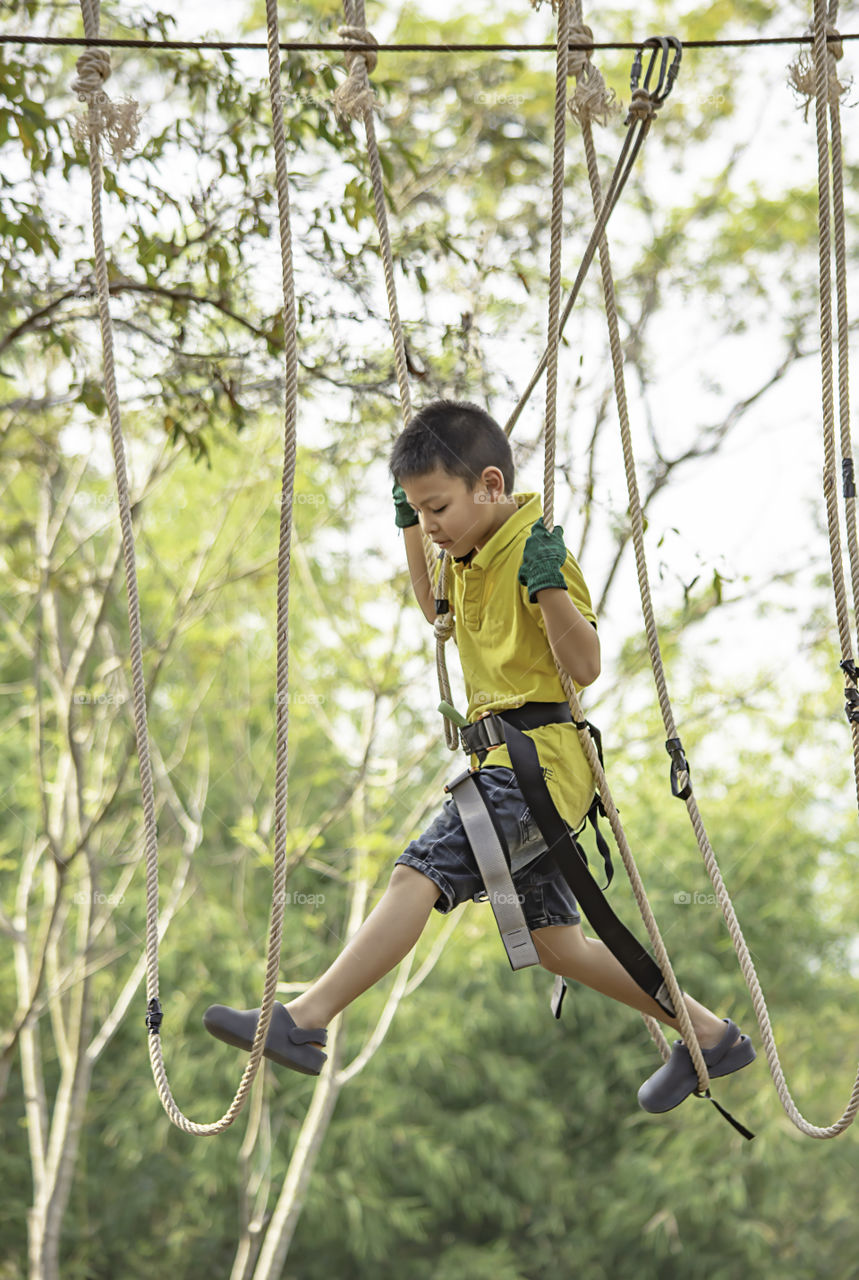 Asean boy nodes the rope and smiling happily in camp adventure Background blurry tree.