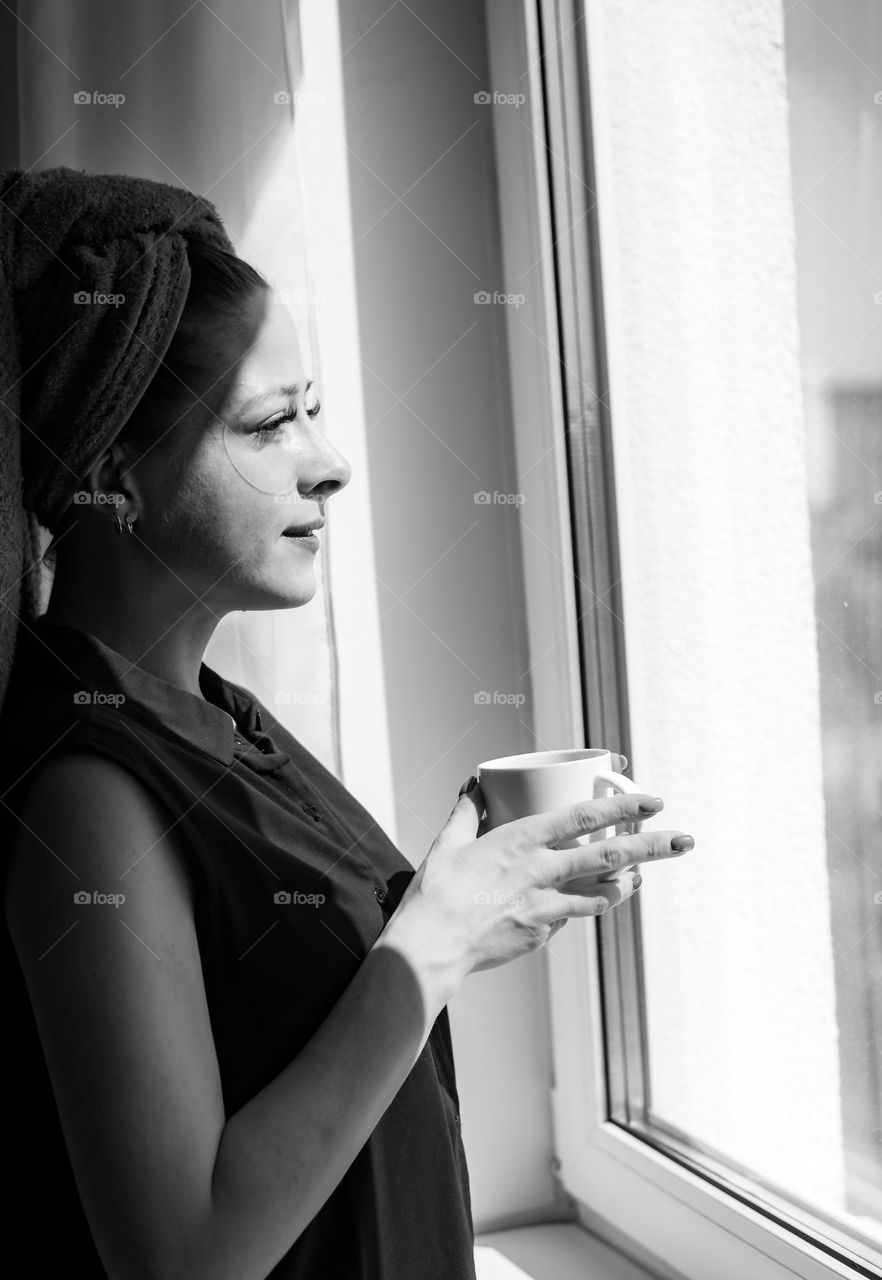 Beautiful woman after shower drinking coffee near window 