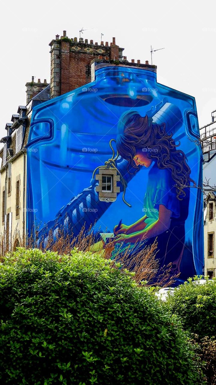 Royal blue wall fresco over the whole side wall of a house in Morlaix, depicting a young girl in a jar taking notes