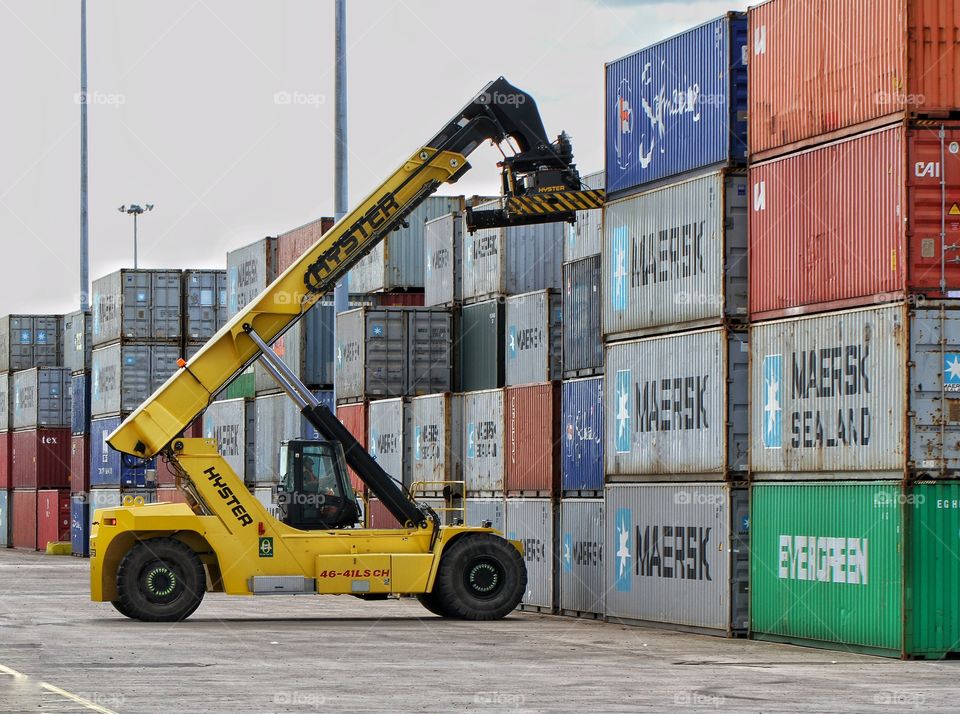 A heavy industry machine lifting a cargo or shipping container into position in a logistics yard.