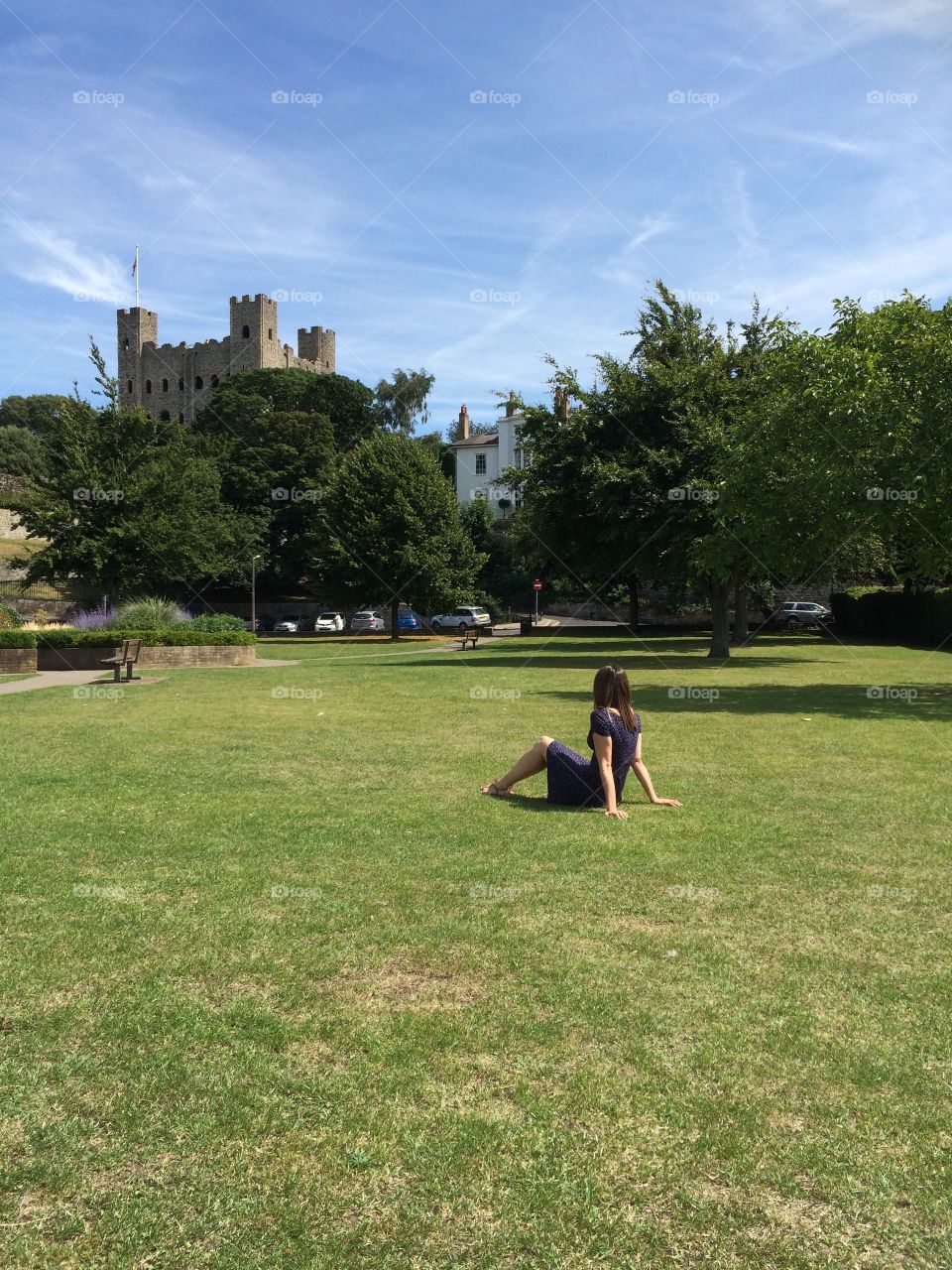 Young women sitting in a lush green park looking at Rochester Castle in the distance. Quintessentially English. Chilling in a park. Relaxing in a park. Looking at the scenery. Daydreaming. Waiting for a prince. Sitting on grass. 