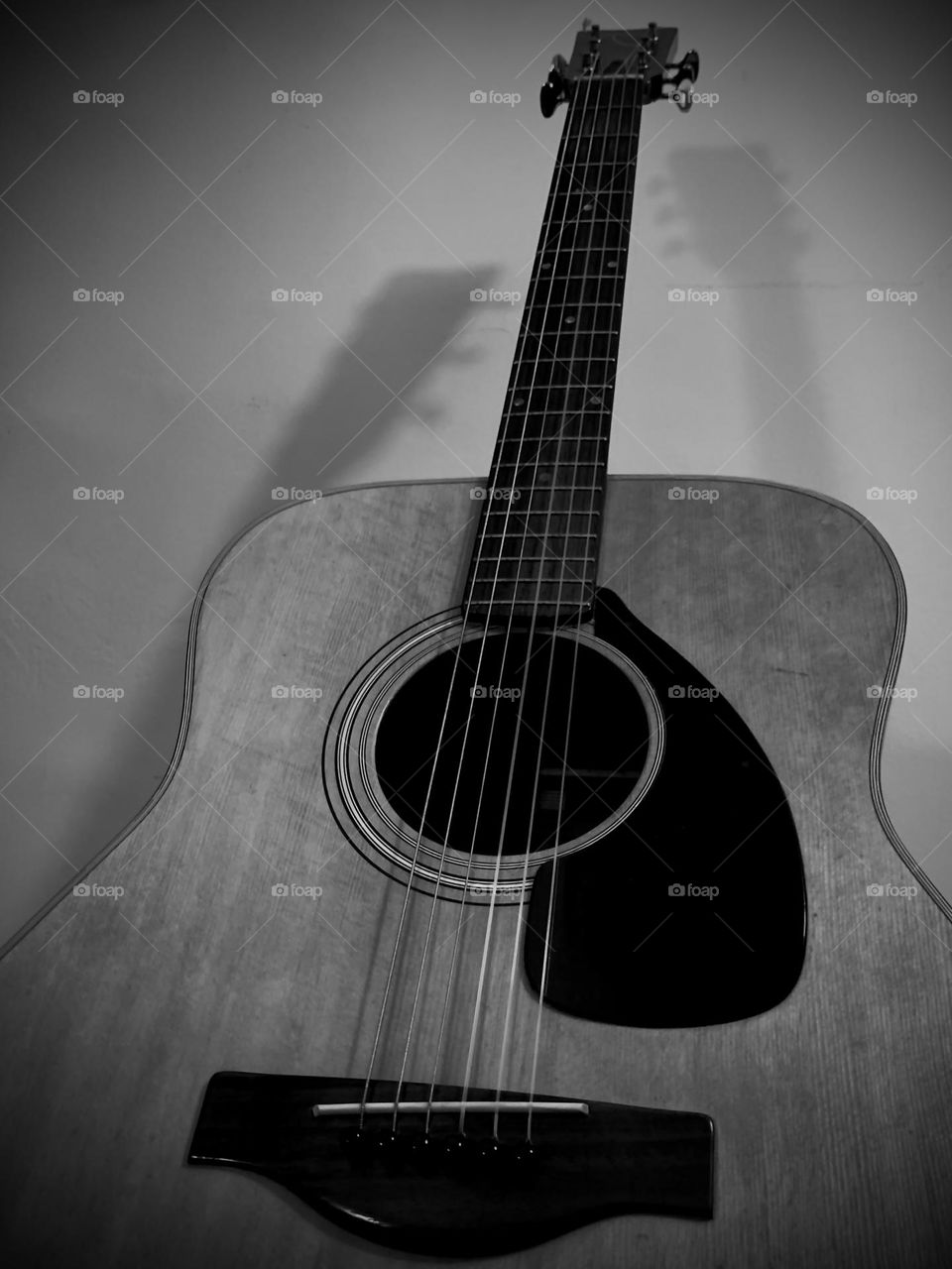 Acoustic guitar leaning on the wall with two shadows. Black and white. 