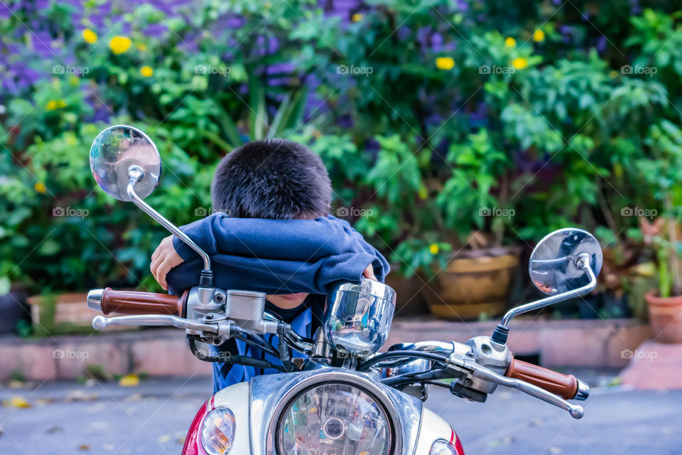 The boy sitting and sleeping on the motorcycle.