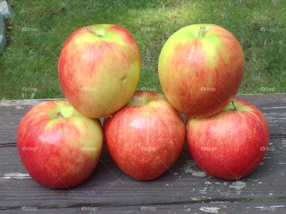 Apples stacked outdoors on wooden bench.