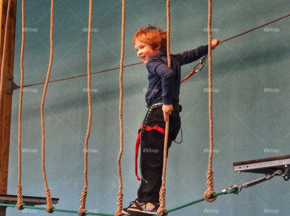 Joy And Confidence. Boy Traversing A Rope Bridge