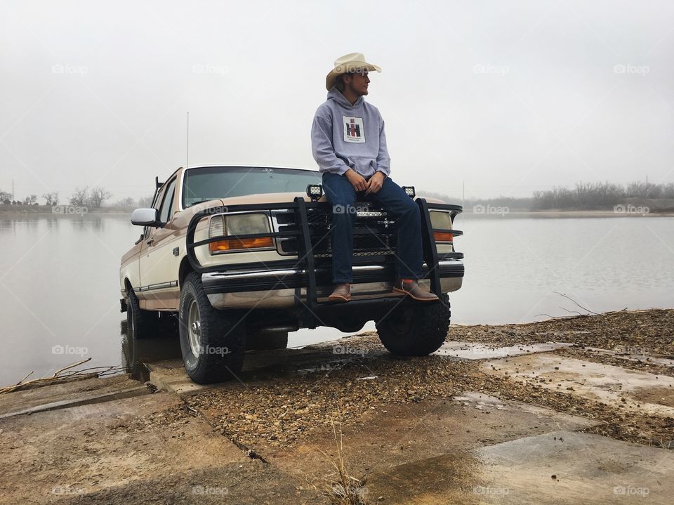 Man wearing hat sitting on car at lake side