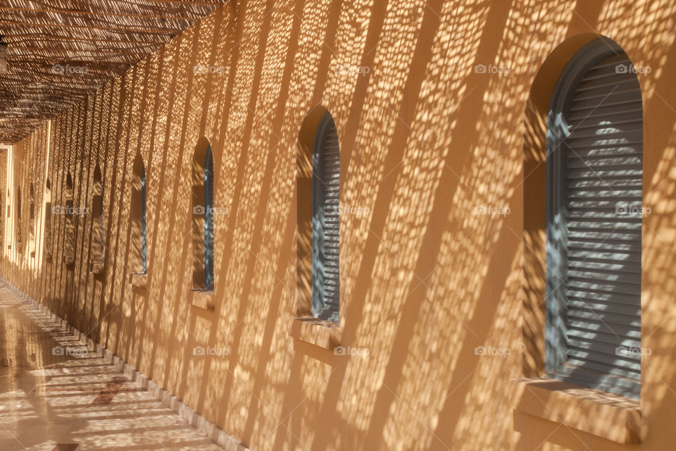 Shadows from straw canopy forming regular pattern on wall with arch windows.