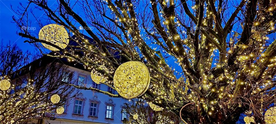 Behind the oversized Christmas tree for the “Christkindlmarkt”, a popular Christmas fair on the “Theresienplatz”, a main square in “Straubing”, “Bavaria” glow beautiful illuminated disks to brighten the holiday season. 2023. Hypnotic Productions