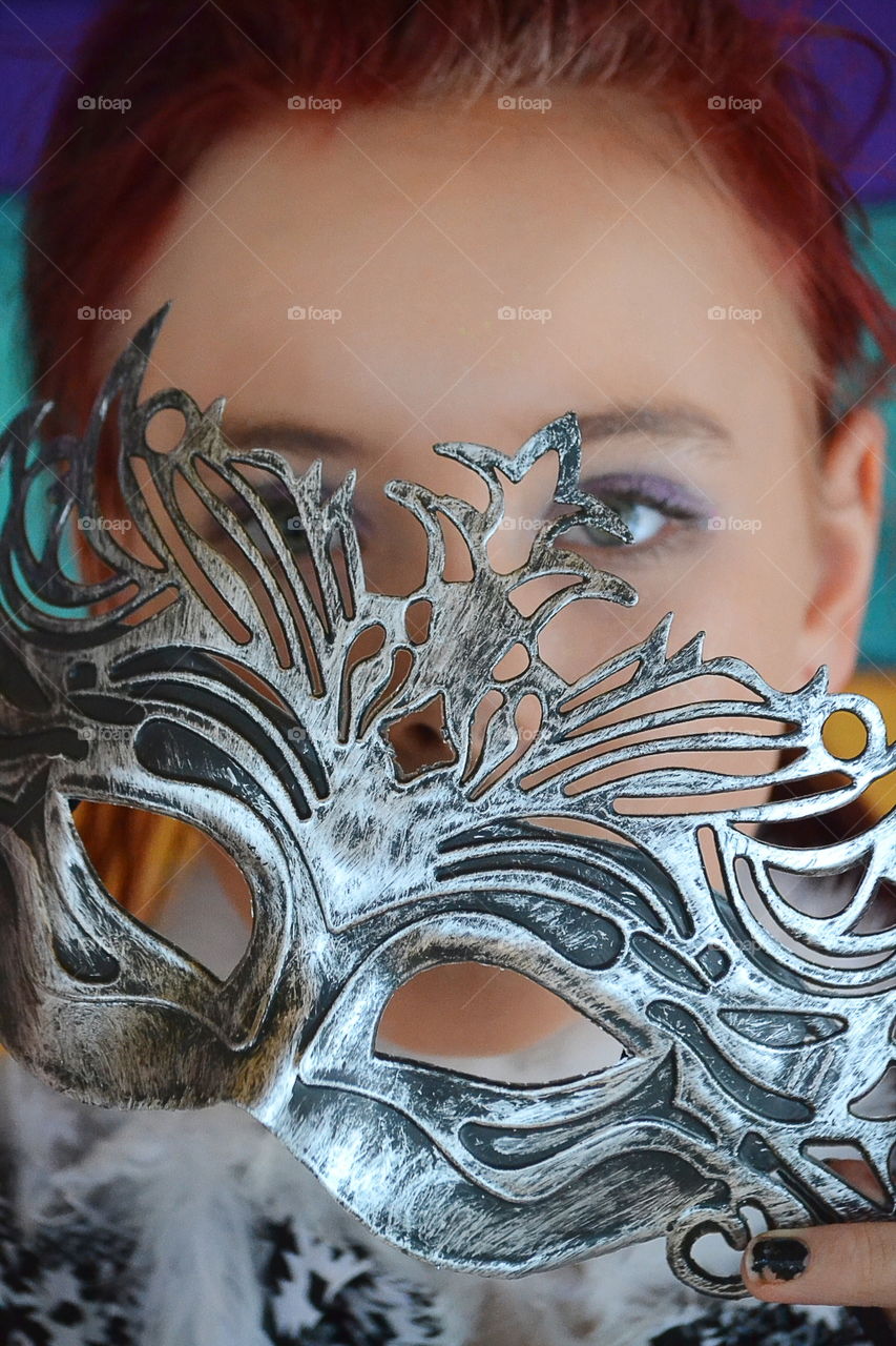 Woman holding carnival mask in front of face