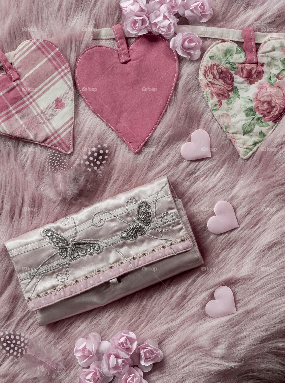 Soft pink flat lay of hearts, paper roses and feathers with satin clutch bag
