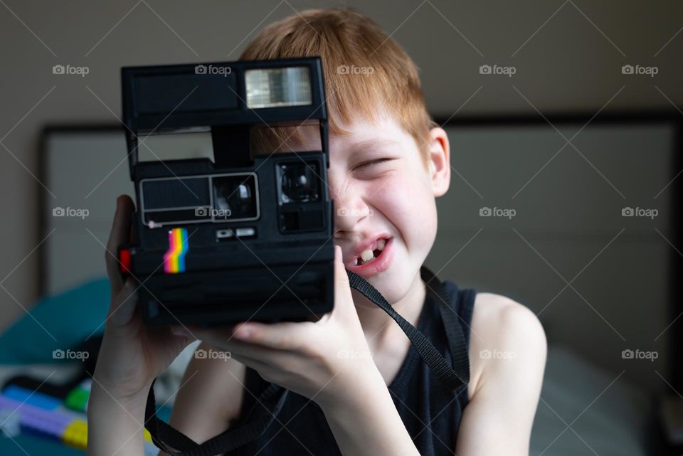 Child red-haired boy with a palaroid camera in his hands, filming life