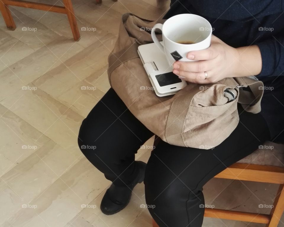 woman sitting and holding phone and coffee