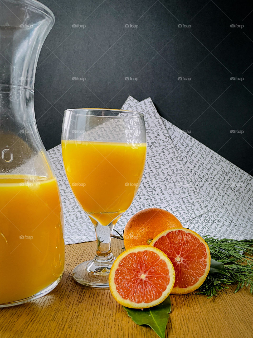 Pitcher and glass of orange juice with orange slices and green foliage. 