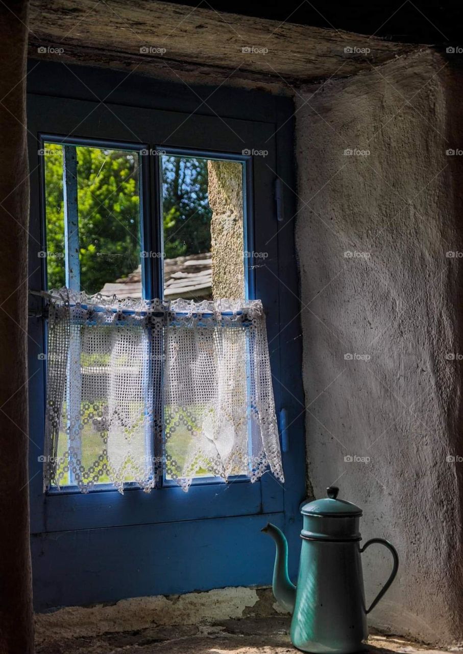 An old green coffee pot on an old bleu window white sill bathed by the light coming through the window panes and frozen for eternity in one of the farmhouses left as they were at the Ecomuseum of Pays of Auray in Saint Dégan