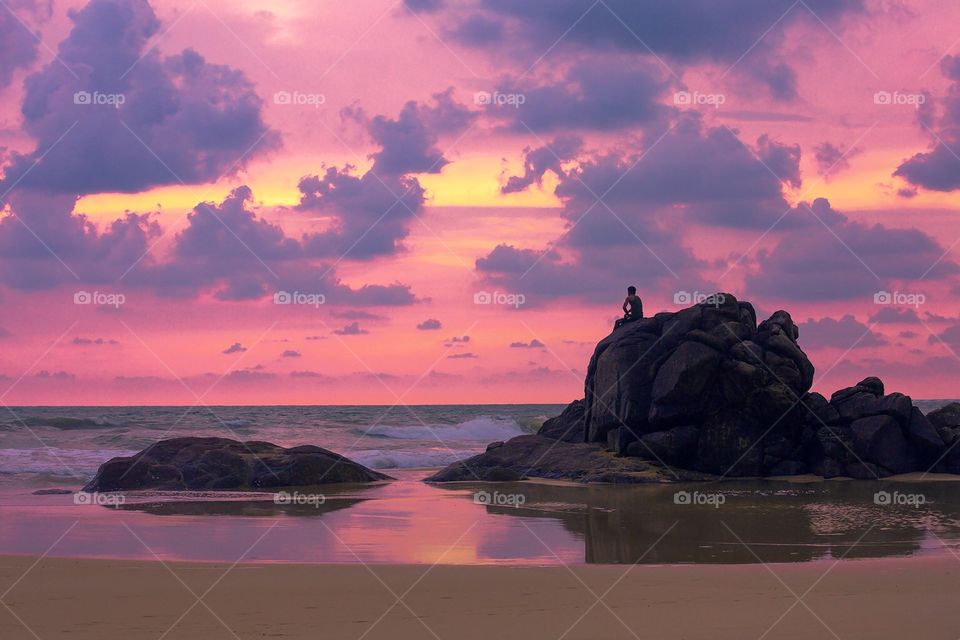 Silhouette of alone man sitting on a big stone near the ocean 