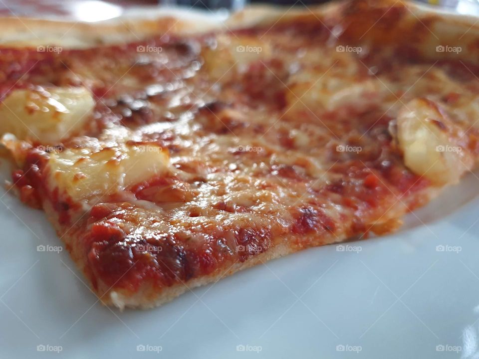 a portrait of a slice of cheese, tomate and pineapple pizza ready to be eaten.