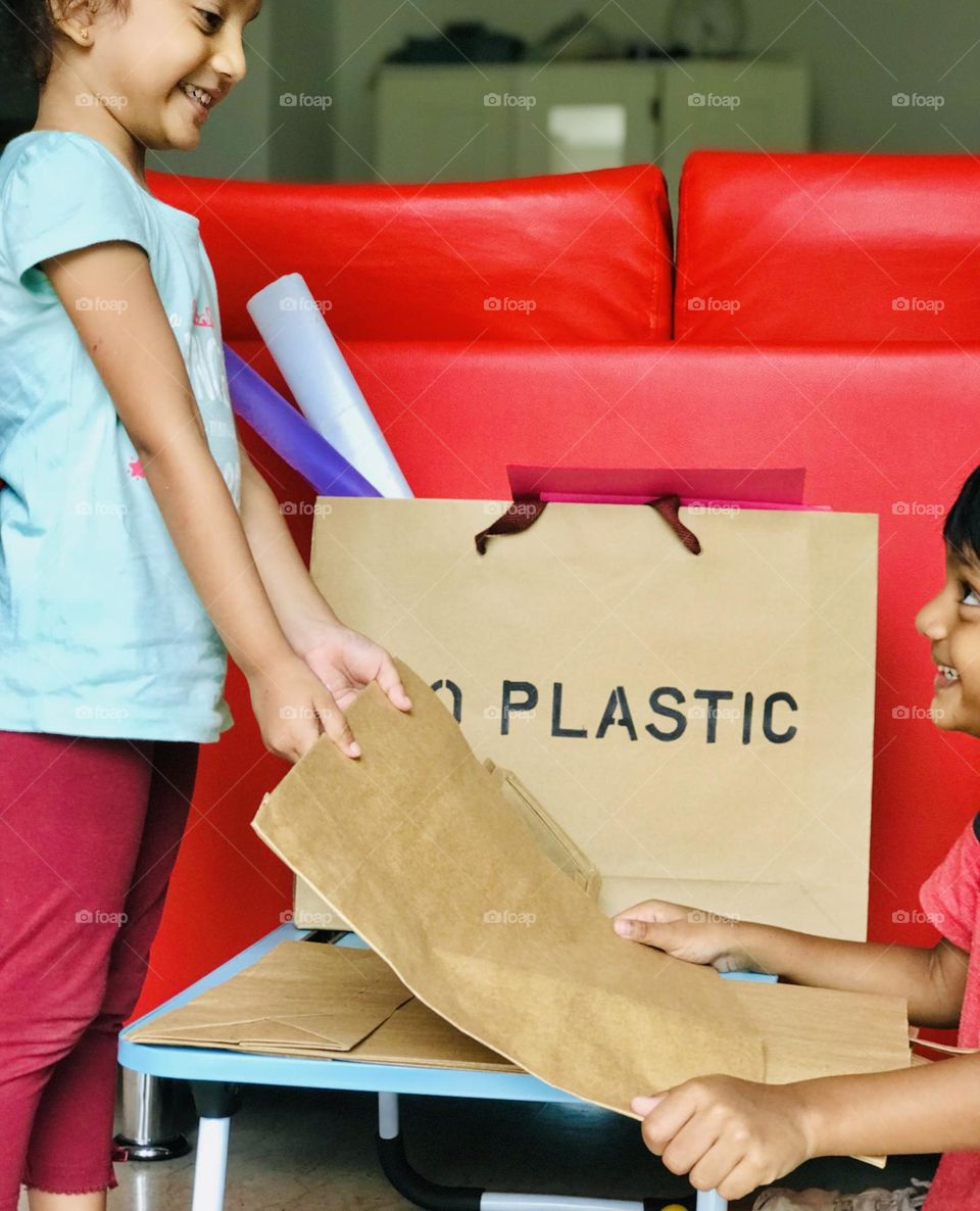 Kids encouraged to use and carry the paper bags instead of using plastic bags.here two kid sharing paper bags and smiling each other.