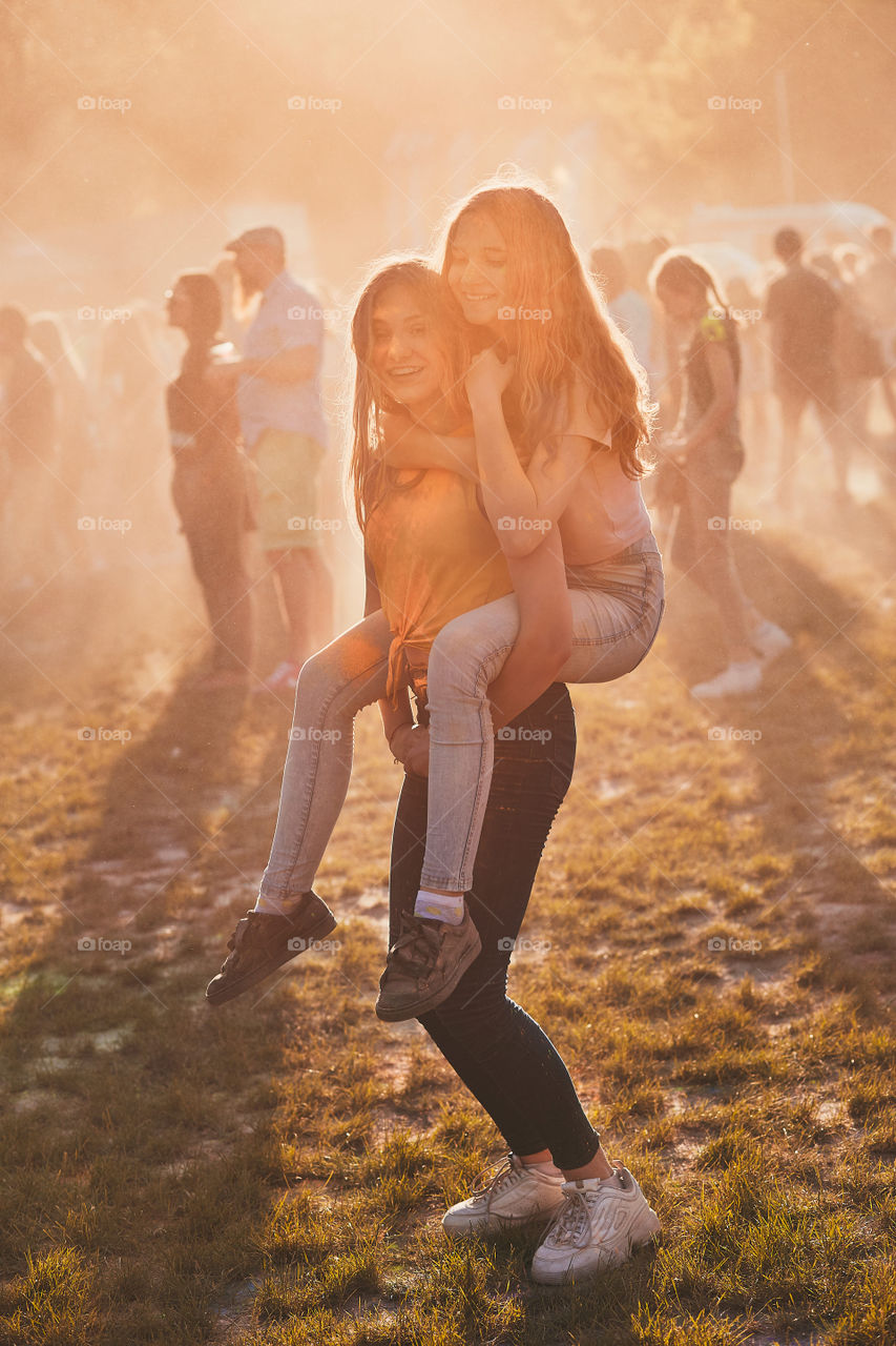 Portrait of happy smiling young girls with colorful paints on faces and clothes. Two friends spending time on holi color festival. Real people, authentic situations