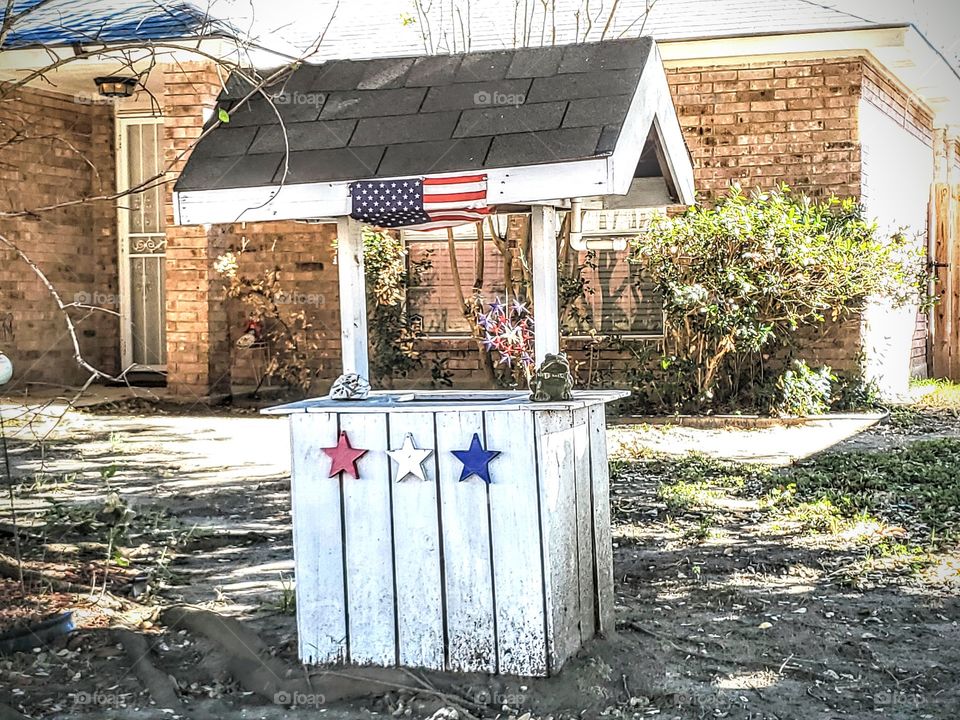 Small American flag on a white wooden well with red white and blue stars in the front yard of a residential home