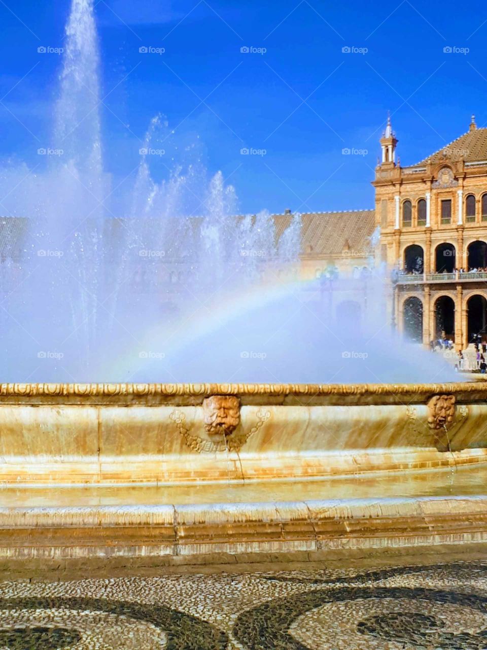 Rainbow in the fountain. Blue skies overhead. Sevilla, Spain. 