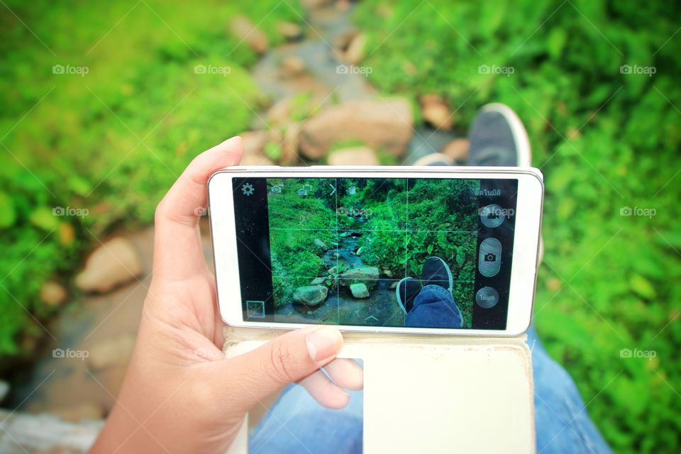 People are sitting and relaxing at the edge of the stream comfortably, and are holding their hands up to take pictures for the memorable experience of this trip.  Love photography.